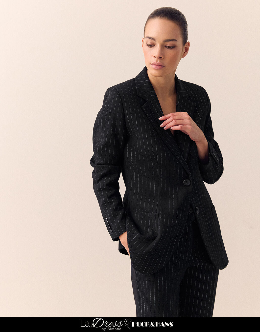 Model standing in the Bombay Black blazer in stretch woven with pinstripes and matching trousers.