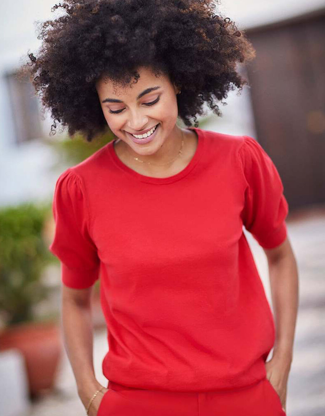 Model standing in the Victoria Red jumper in organic cotton knit with short puff sleeves.