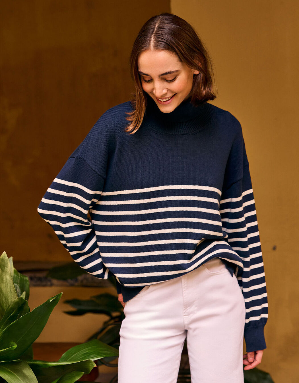 Model standing in the Cecile Midnight Blue Ivory Stripe jumper in organic cotton knit with white jeans.