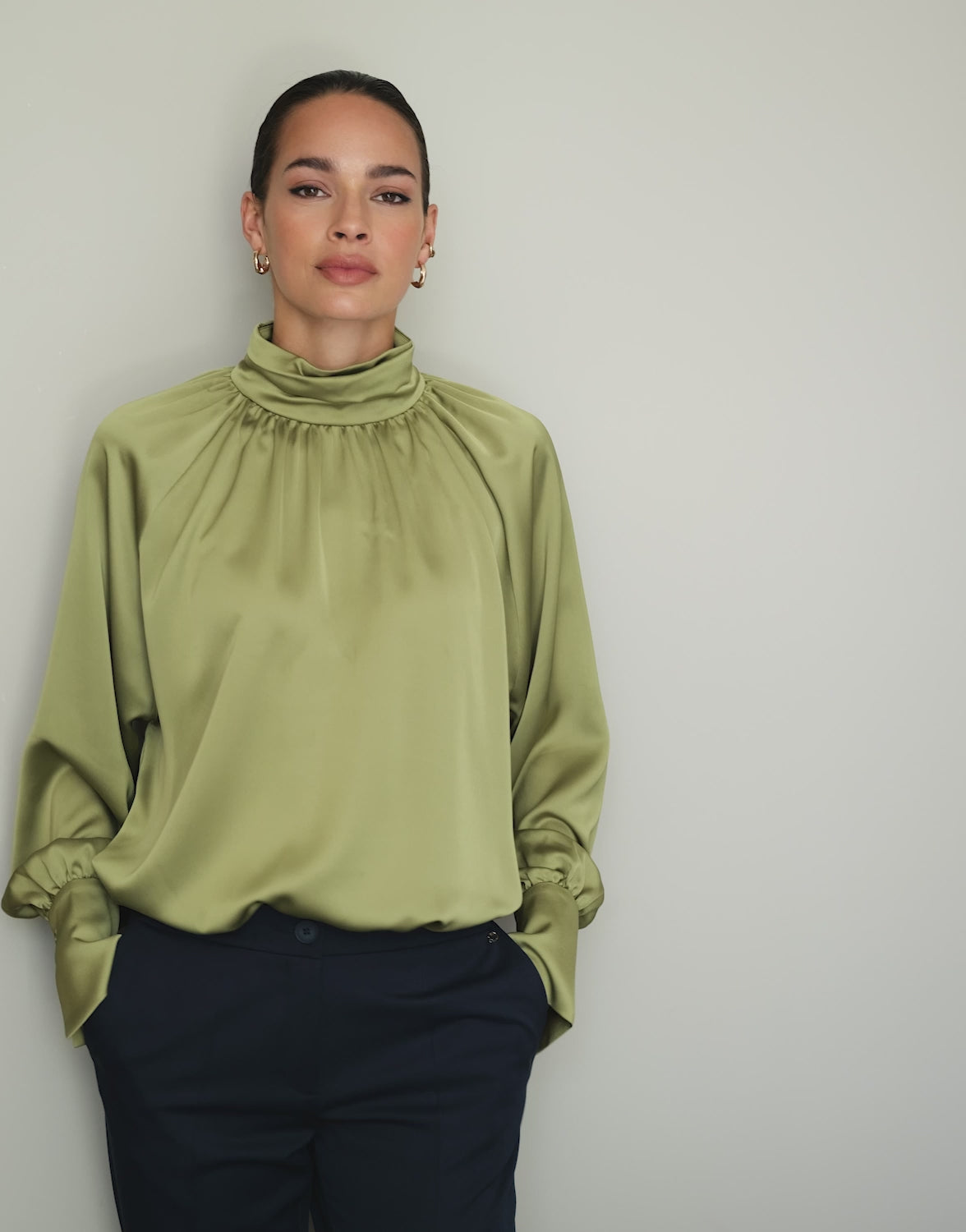 Video of a model wearing the Alix Lime satin blouse with a high gathered neck, back view.