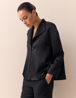 Model standing in the Sao Paulo Black Satin jacket in crepe satin with a wide collar.